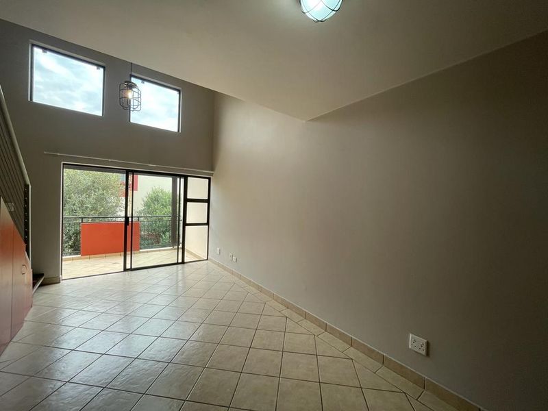 Spacious, empty living area featuring double volume ceilings, tiled floors, and large sliding doors leading to a private balcony.