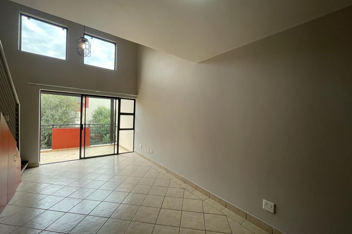 Spacious, empty living area featuring double volume ceilings, tiled floors, and large sliding doors leading to a private balcony.