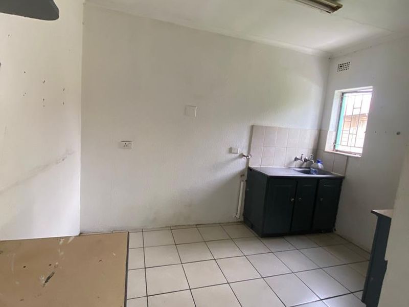 A basic, empty kitchen area featuring tiled flooring, a single sink unit with base cabinetry, and a tiled splashback.