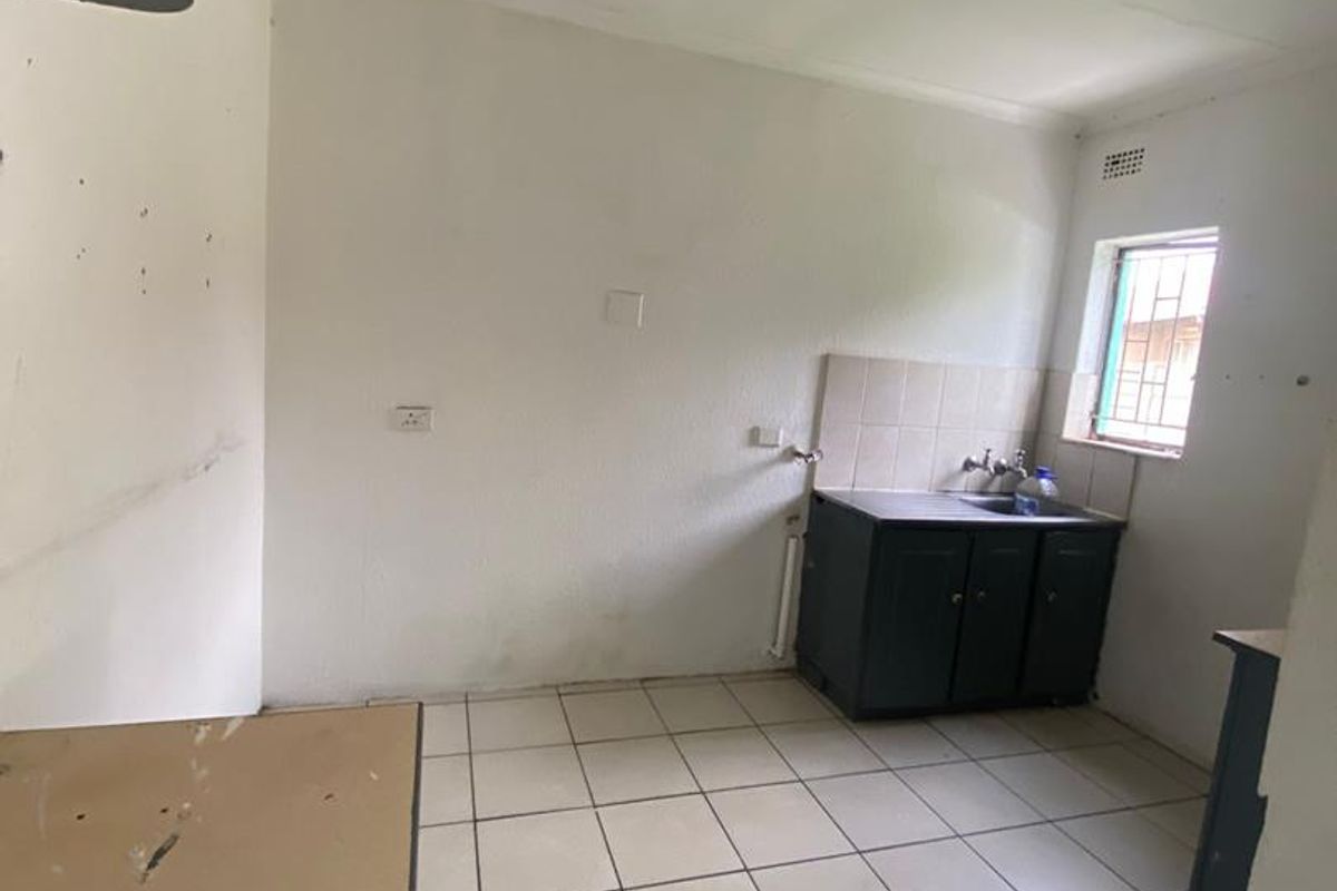 A basic, empty kitchen area featuring tiled flooring, a single sink unit with base cabinetry, and a tiled splashback.