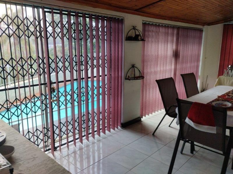 Dining area featuring tiled flooring, timber ceiling, and sliding glass doors with security gates, offering a view of the outdoor pool area.
