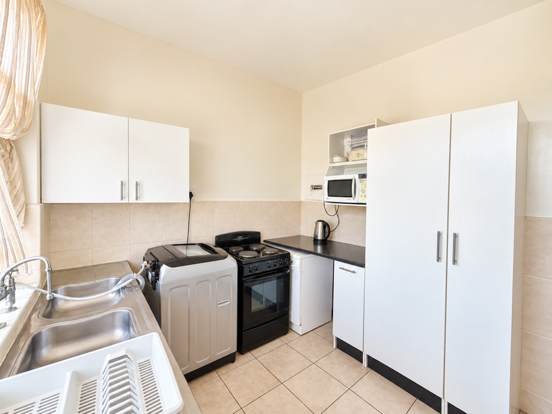 A functional kitchen featuring white cabinetry, tiled backsplash, double stainless steel sink, and a freestanding stove with integrated microwave storage.