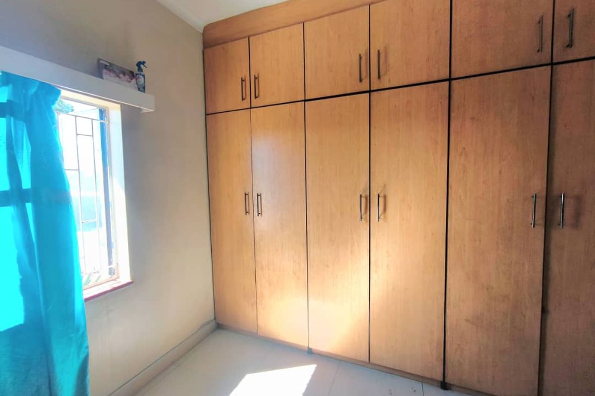 A bedroom featuring extensive floor-to-ceiling built-in wooden cupboards and a window fitted with security bars.