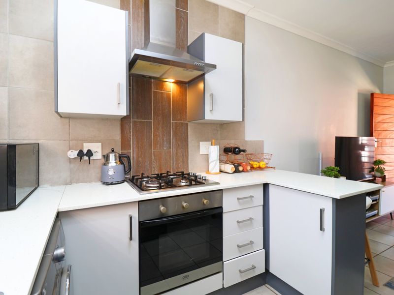 Modern kitchen featuring sleek white cabinetry, stone countertops, a gas hob, and a stainless steel extractor fan with stylish tiled backsplash.