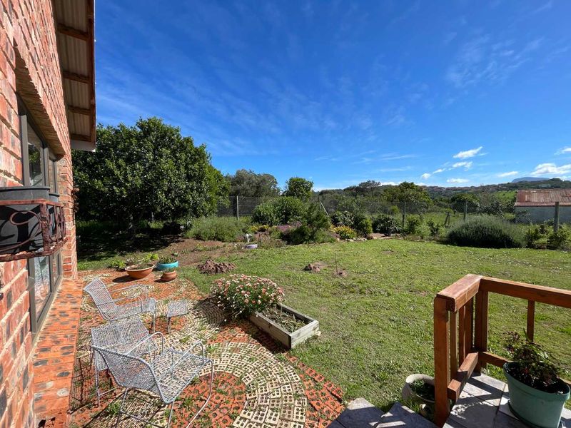 A rear garden view featuring an exposed brick exterior wall, a paved patio area with timber railing, and a spacious lawn with established landscaping.