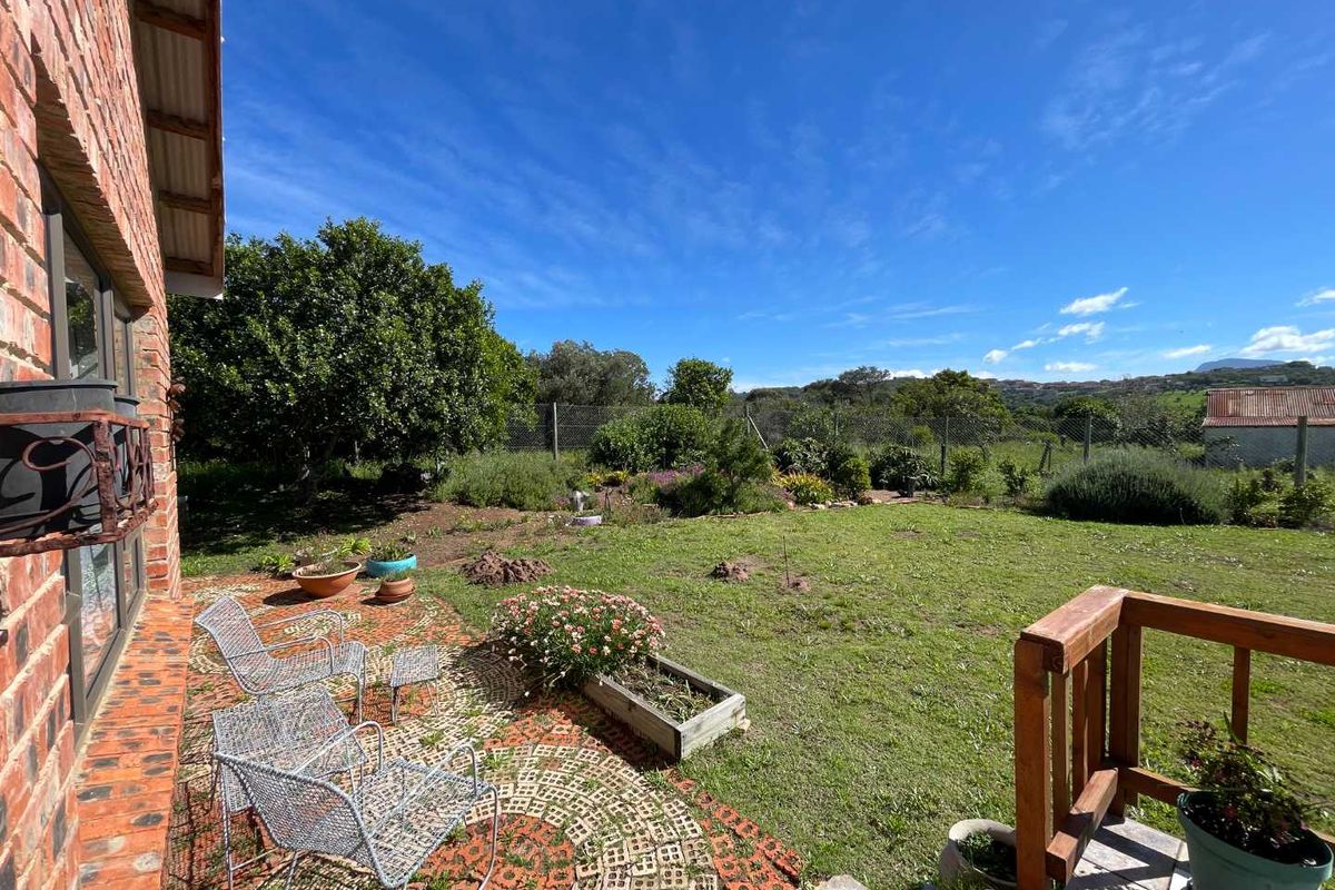 A rear garden view featuring an exposed brick exterior wall, a paved patio area with timber railing, and a spacious lawn with established landscaping.