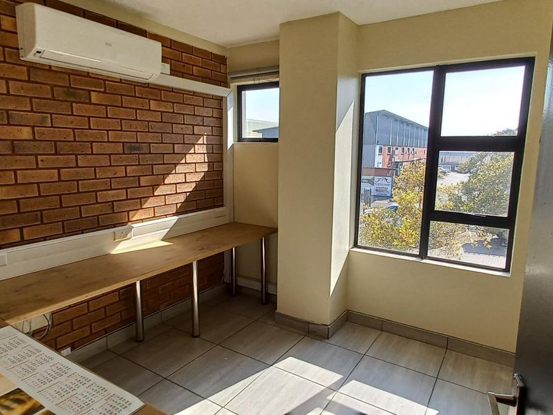 A functional office space featuring an exposed brick feature wall, built-in wooden desk, tiled flooring, and a wall-mounted air conditioning unit.