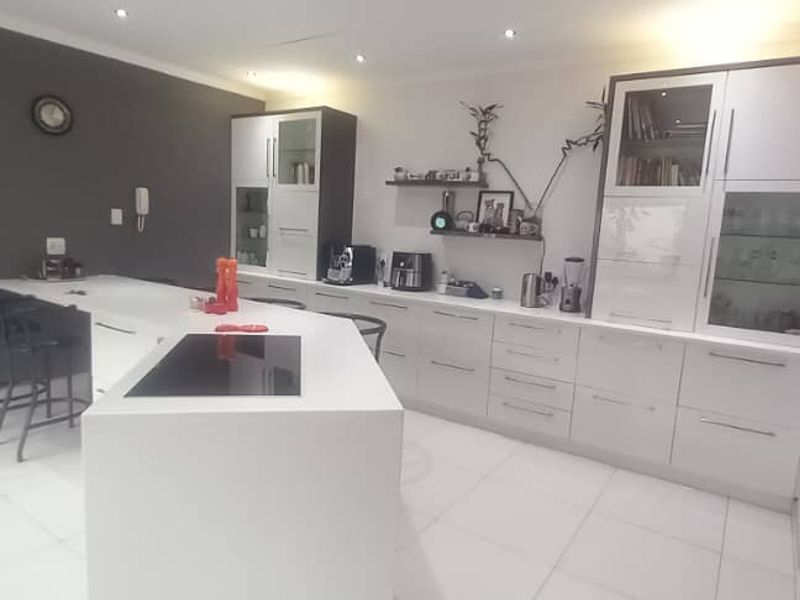 Modern kitchen featuring a central island with integrated hob, sleek white cabinetry, and tiled flooring, offering a clean and functional culinary space.