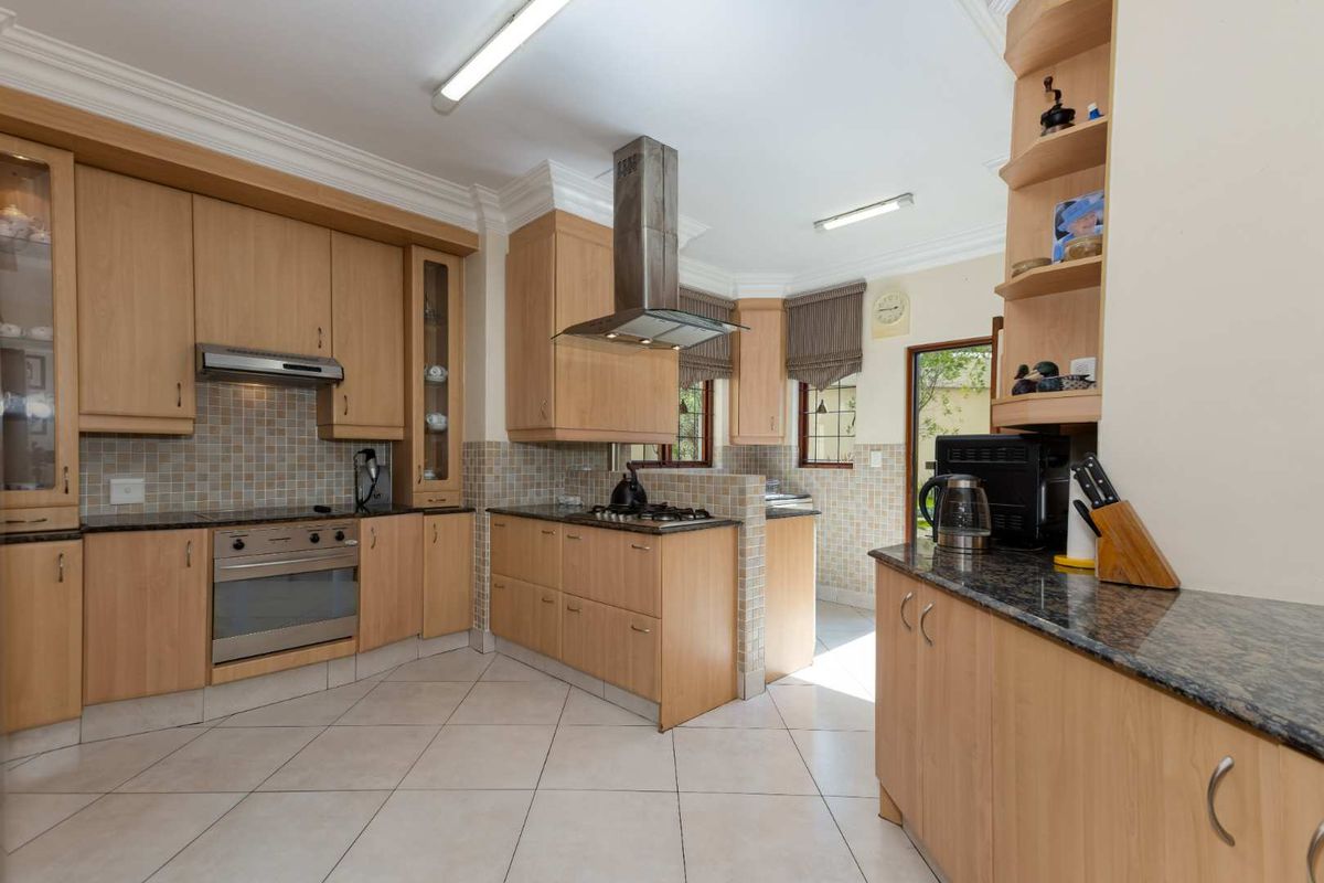 Spacious kitchen featuring light wood cabinetry, granite countertops, mosaic tile backsplash, stainless steel extractor fan, and tiled flooring with direct access to the garden.