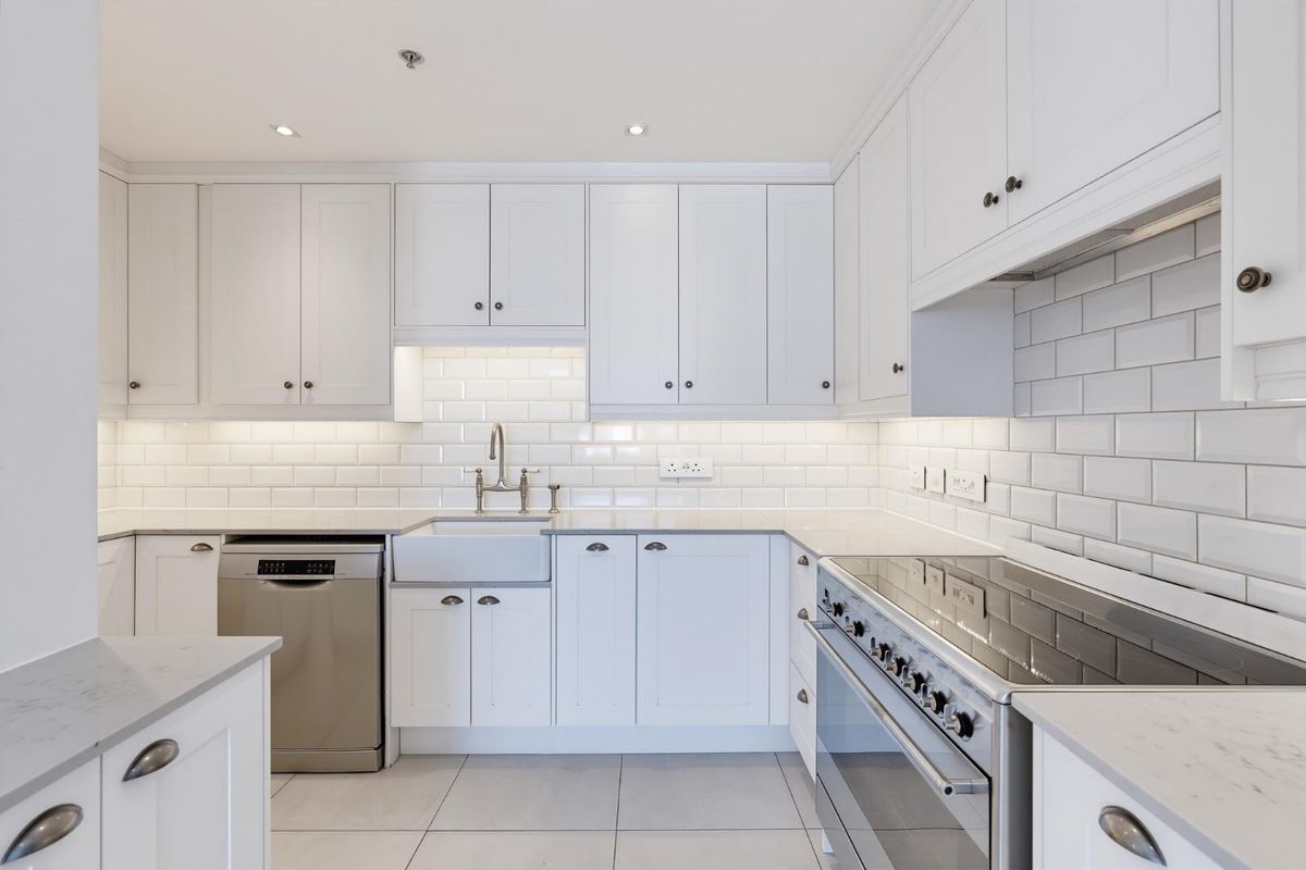 Modern kitchen featuring white shaker-style cabinetry, subway tile backsplash, farmhouse sink, stone countertops, and high-quality stainless steel appliances.