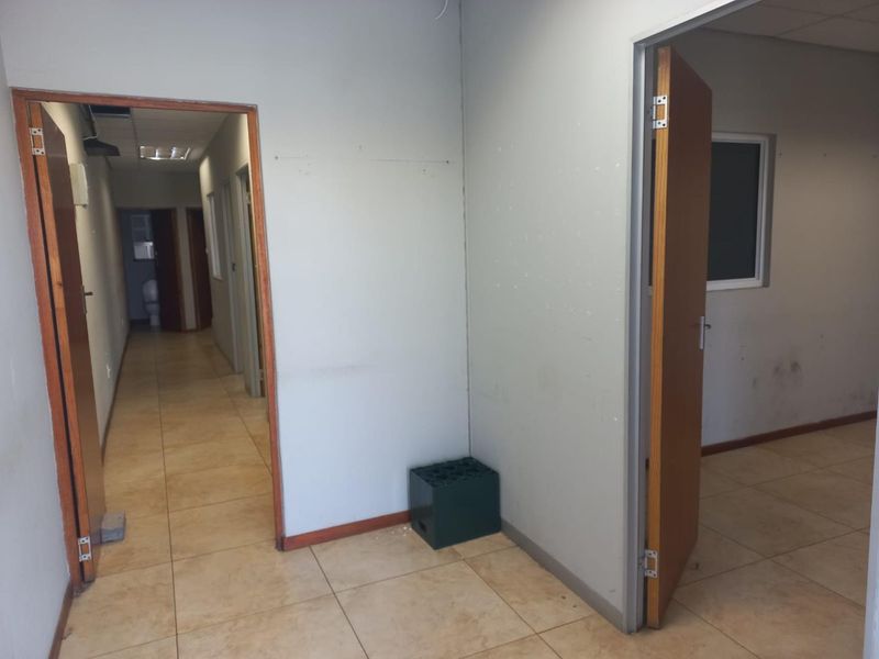 A vacant office hallway featuring tiled flooring, wooden door frames, and neutral wall finishes, providing access to multiple rooms.
