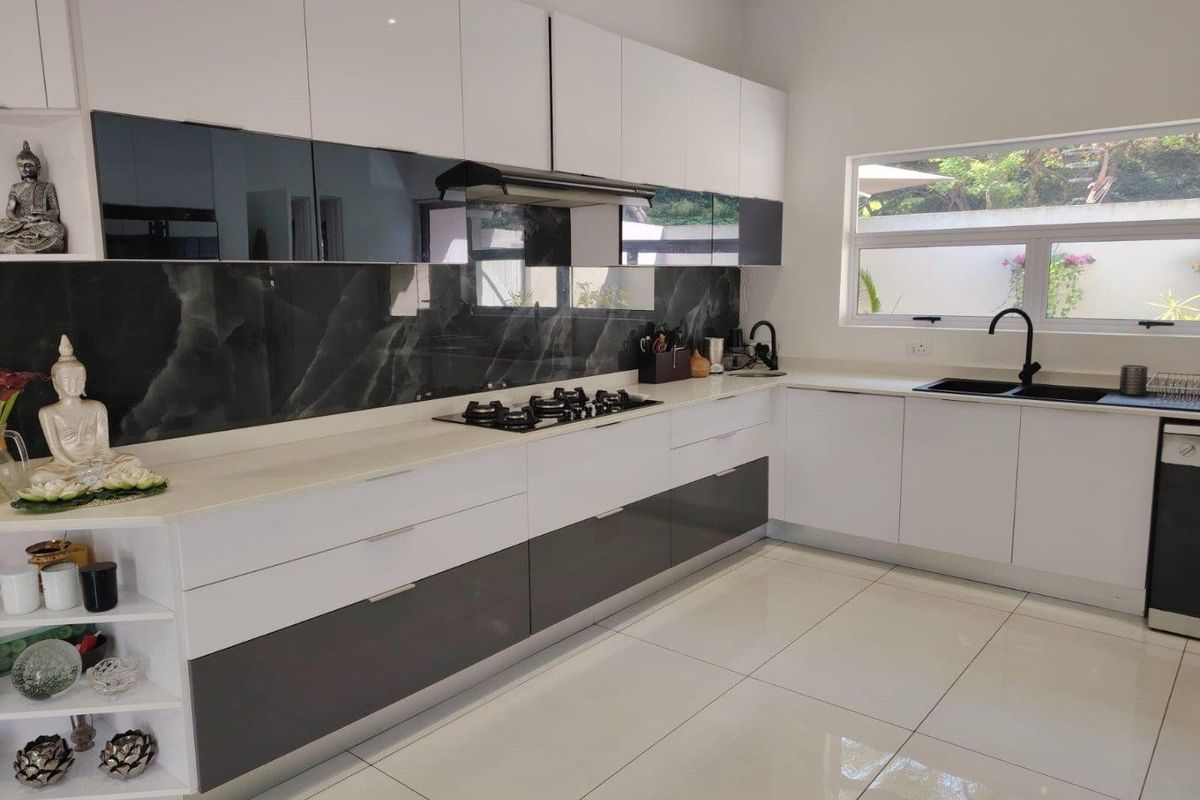 Modern kitchen featuring high-gloss cabinetry, stone countertops, a gas hob with extractor, and a stylish marble-look splashback with black fixtures.