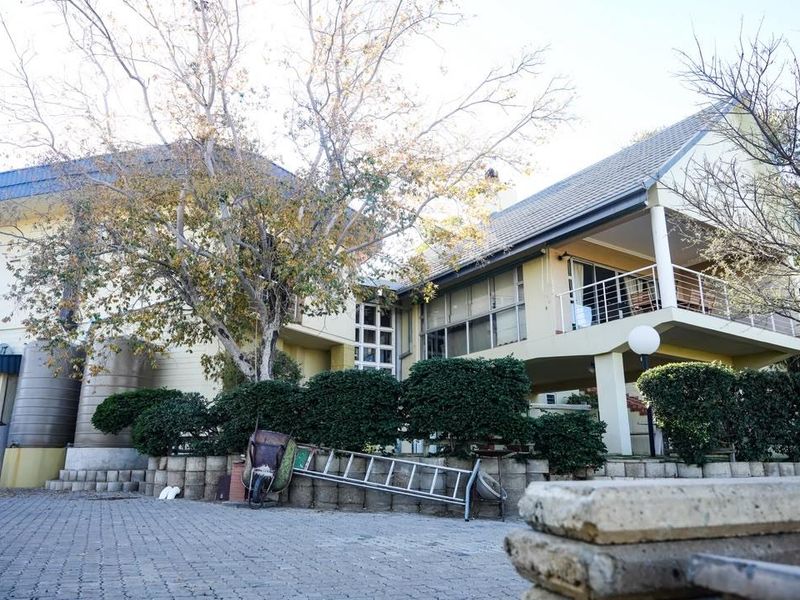 Rear view of a multi-level house featuring a balcony, paved driveway, and large water storage tanks set against a landscaped garden area.