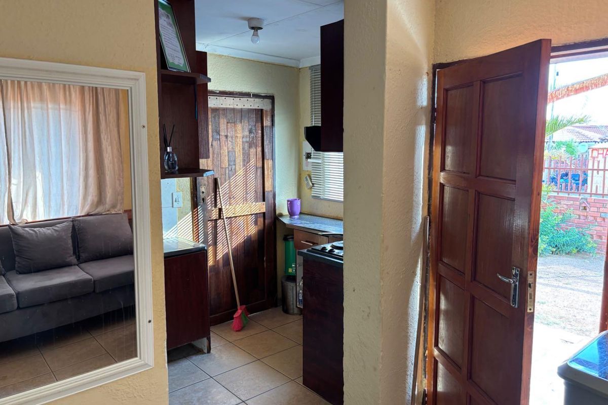 A view from the entrance into a compact kitchen area featuring dark wood cabinetry and tiled flooring, leading to an exterior doorway.
