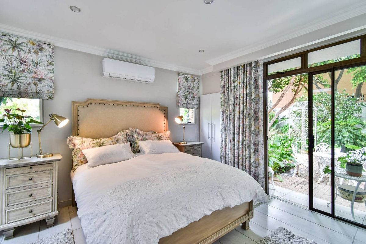 A bright bedroom featuring tiled flooring, recessed ceiling lighting, a wall-mounted air conditioning unit, and sliding glass doors opening to a private garden patio.