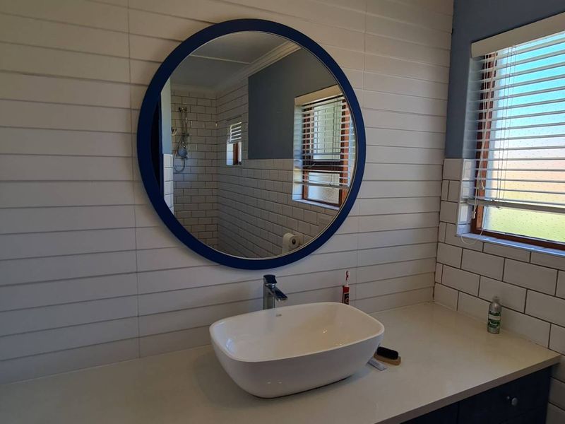 A modern bathroom featuring a vessel sink on a vanity countertop, subway tile backsplash, and horizontal wall cladding with a circular mirror.