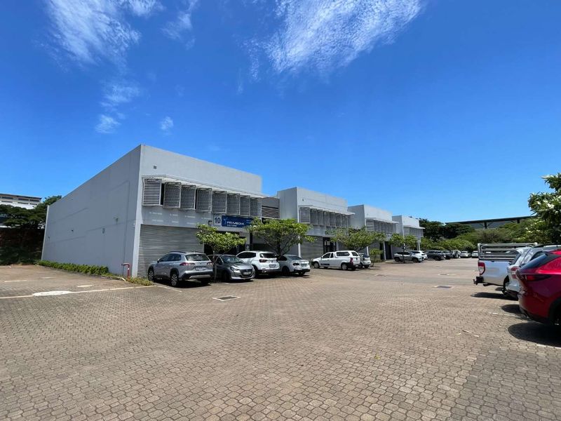 Exterior view of a modern commercial complex featuring paved parking, roller shutter doors, and functional louvre window shutters.