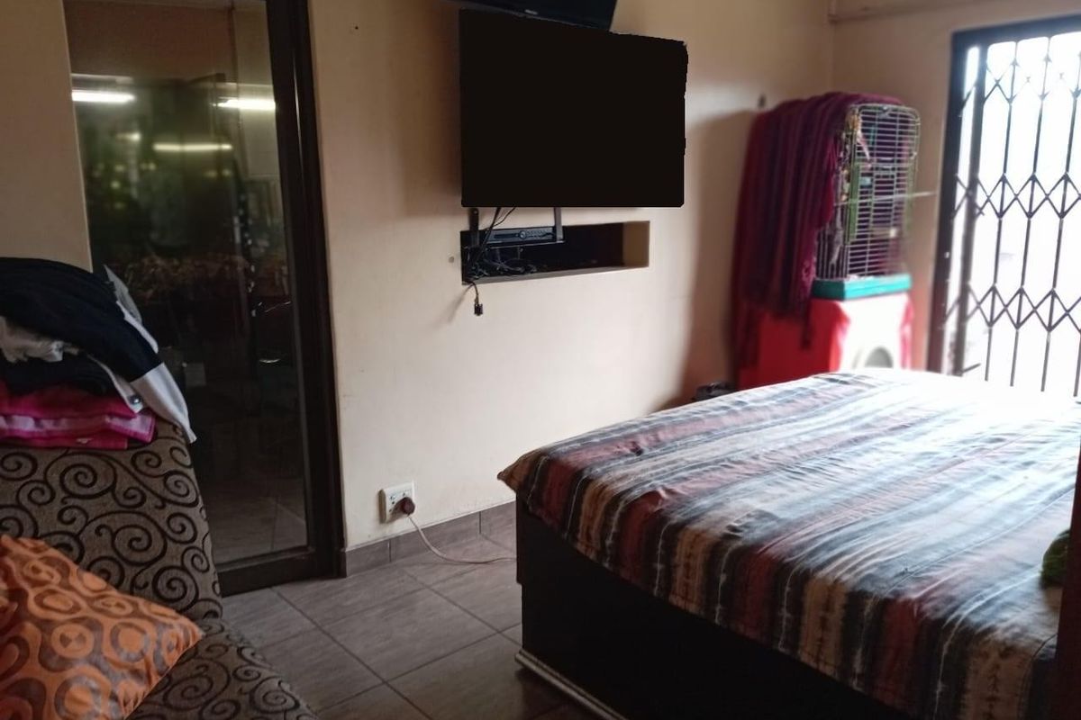 A bedroom featuring tiled flooring, a security gate on the window, and a recessed wall niche for media equipment.