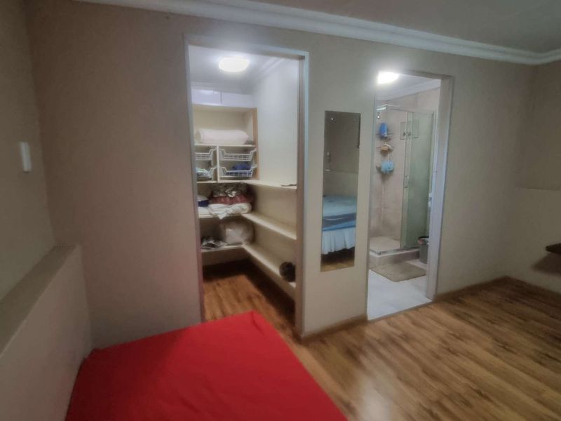 Bedroom featuring laminate flooring, an integrated walk-in closet with built-in shelving, and an en-suite bathroom with a glass shower enclosure.