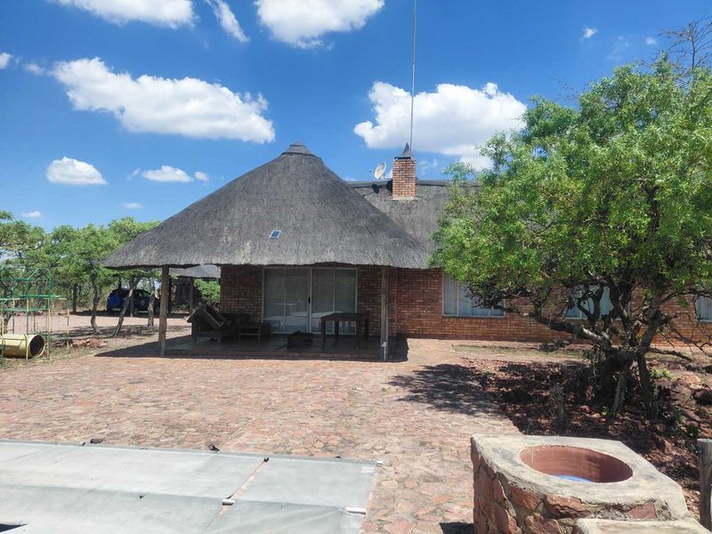 Rear view of a house featuring a thatched roof, brick facade, covered patio area, and a stone-paved outdoor space with a built-in braai.