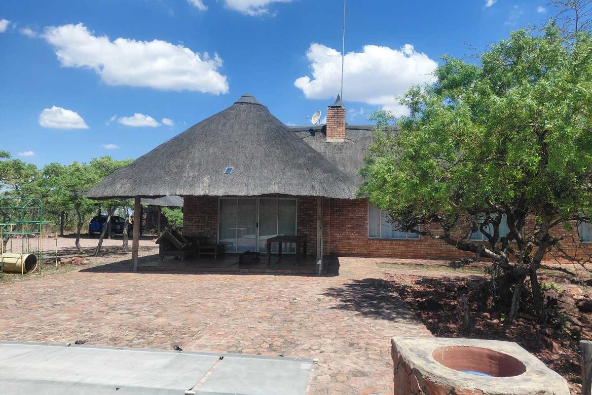 Rear view of a house featuring a thatched roof, brick facade, covered patio area, and a stone-paved outdoor space with a built-in braai.