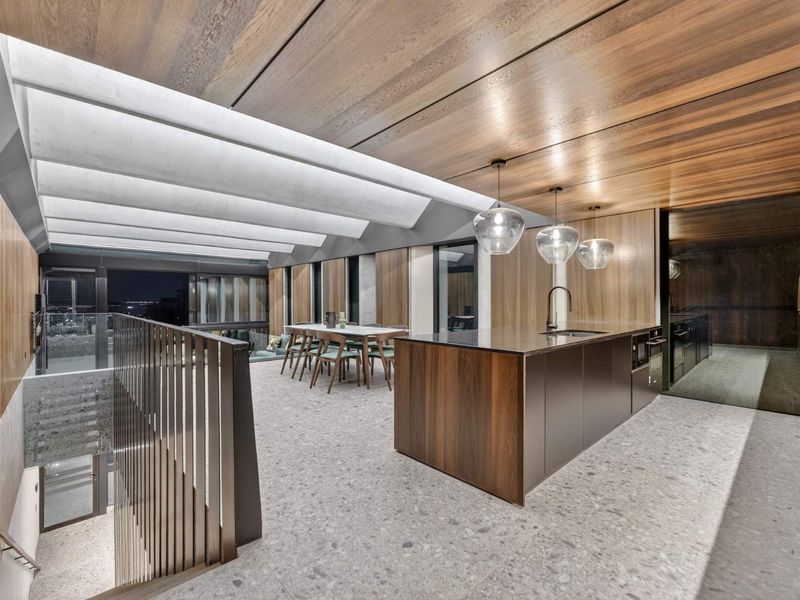 Modern open-plan living and kitchen area featuring high-end timber ceiling finishes, terrazzo flooring, and a sleek central kitchen island with integrated appliances.