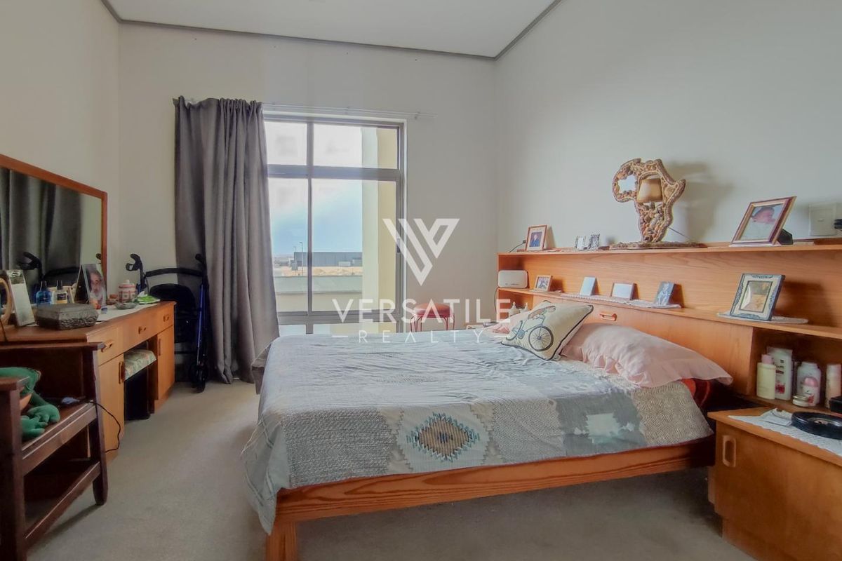 A bedroom featuring a large window with access to a balcony, neutral carpeting, and built-in headboard shelving.