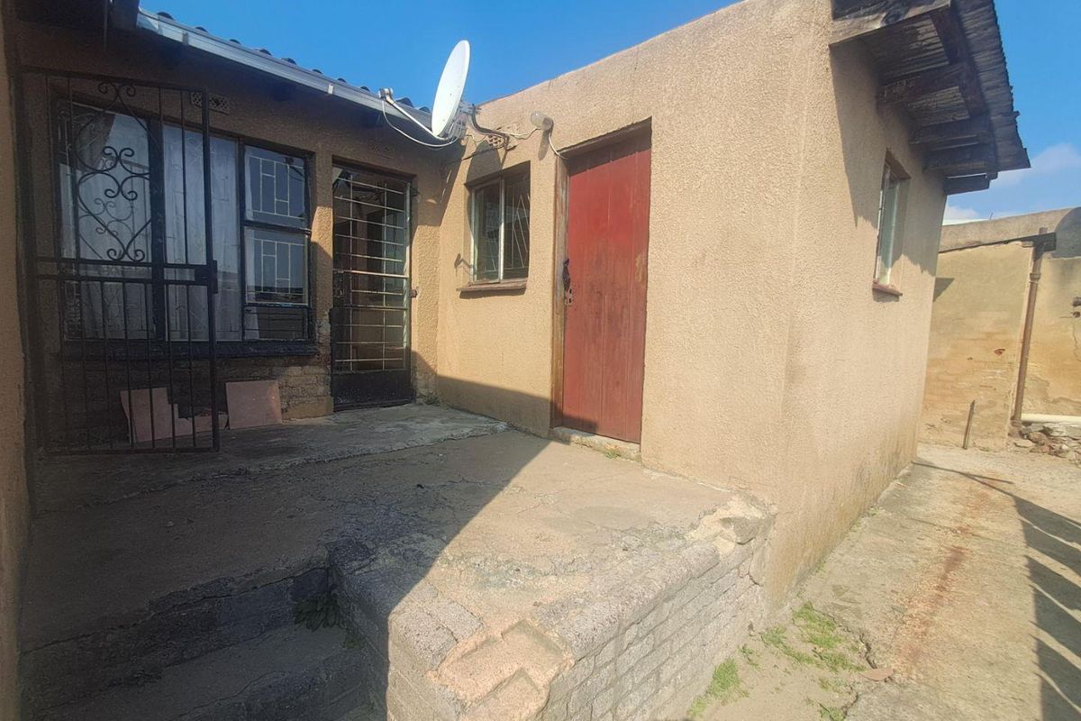Exterior view of the rear of the house featuring a concrete patio area, security gates, and access doors.