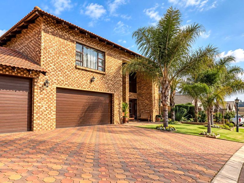 A well-maintained double-story brick home featuring a spacious paved driveway, double garage, and established garden landscaping.