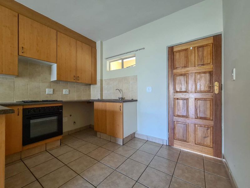 A functional kitchen featuring wooden cabinetry, built-in oven, tiled backsplash, and tiled flooring, offering a clean and practical space ready for updates.