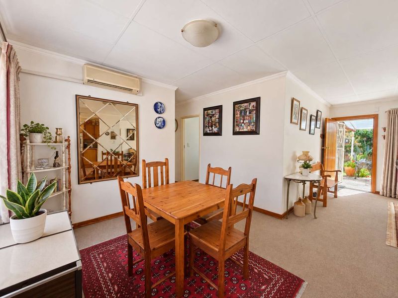 A well-maintained living and dining area featuring neutral walls, carpeted flooring, and a wall-mounted air conditioning unit, with direct access to the outdoor space.