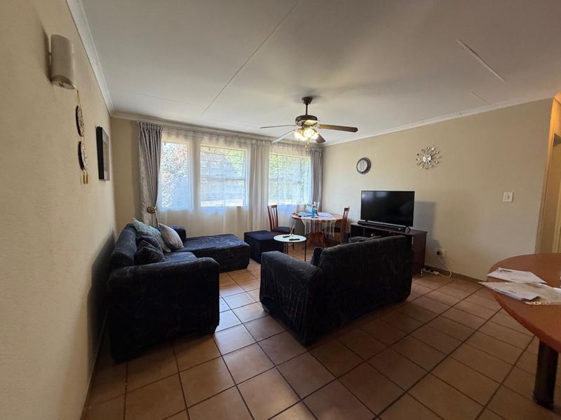 A functional living room featuring tiled flooring, a ceiling fan, and large windows with security bars, offering a comfortable and practical living space.