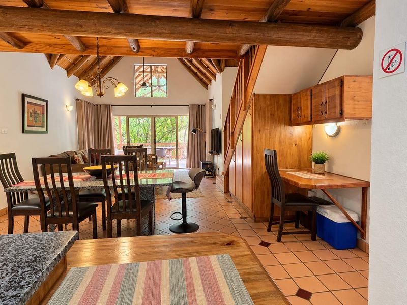 Spacious open-plan living and dining area featuring exposed timber beams, tiled flooring, and direct access to an outdoor patio through sliding glass doors.