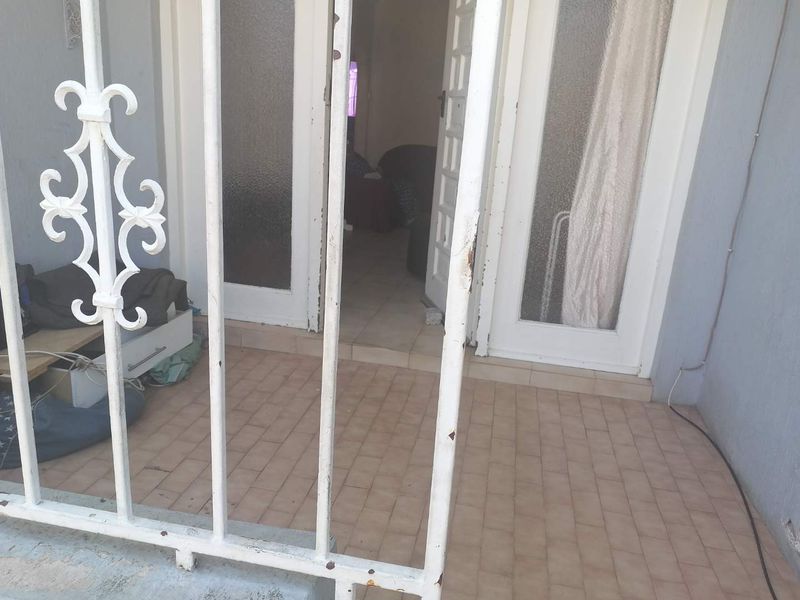 A small covered patio area featuring tiled flooring and a white wrought iron security gate leading to the main entrance.