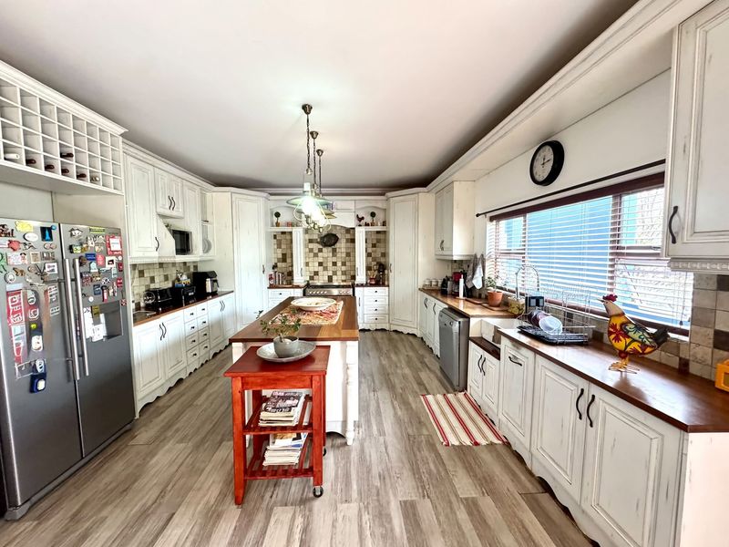 Spacious kitchen featuring white cabinetry, wooden countertops, a central island, tiled backsplash, and ample storage with an integrated dishwasher.