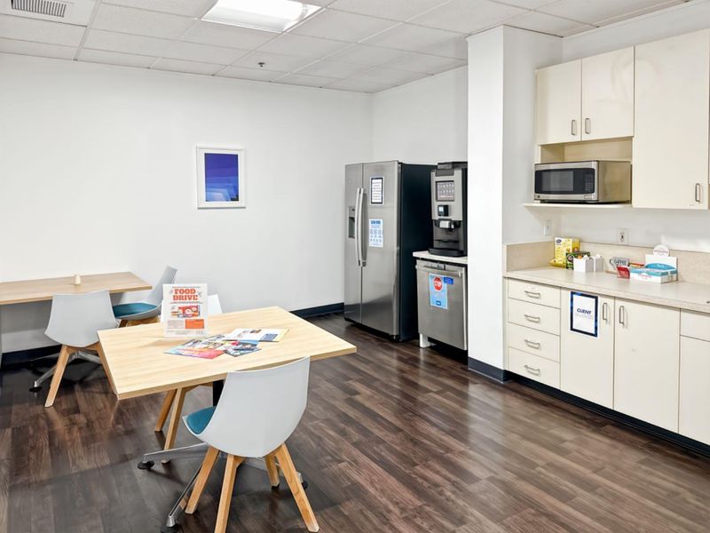 Office breakroom featuring laminate cabinetry, built-in microwave, vinyl plank flooring, and a drop ceiling, providing a functional space for staff.