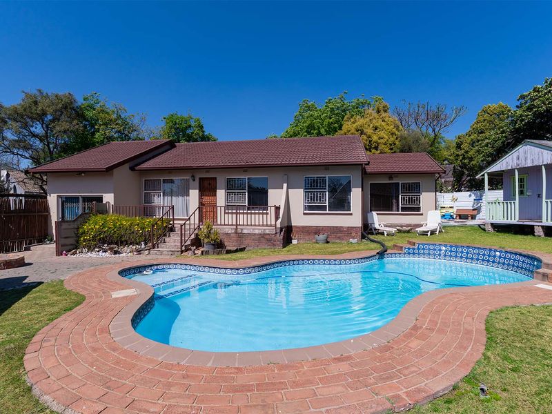 Rear exterior view of the house featuring a swimming pool, brick paved surround, and a separate outbuilding in the garden.