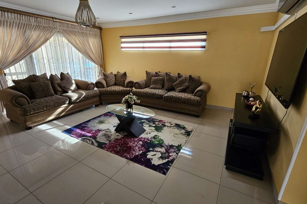 A spacious living room featuring large format floor tiles, recessed ceiling lighting, and a wall-mounted television setup.