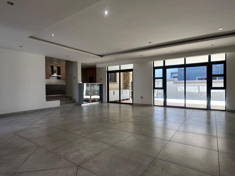 Spacious open-plan living area featuring large format floor tiles, recessed ceiling lighting, and seamless access to the outdoor patio through sliding glass doors.