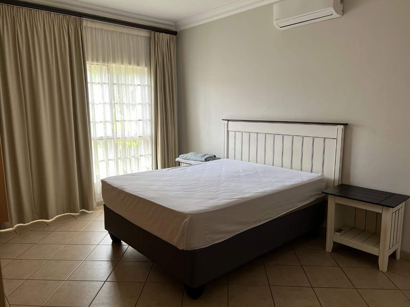 A well-maintained bedroom featuring tiled flooring, a split-system air conditioner, and large sliding glass doors with curtains for natural light.