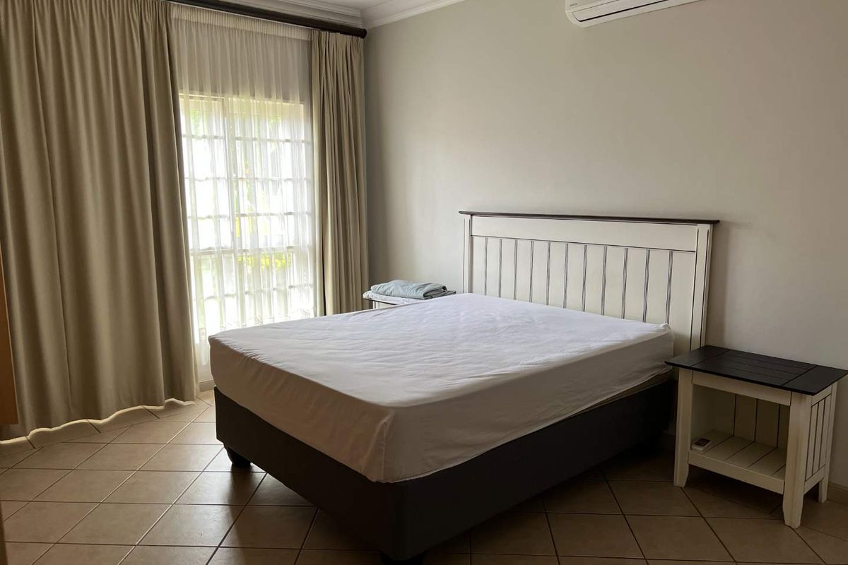 A well-maintained bedroom featuring tiled flooring, a split-system air conditioner, and large sliding glass doors with curtains for natural light.