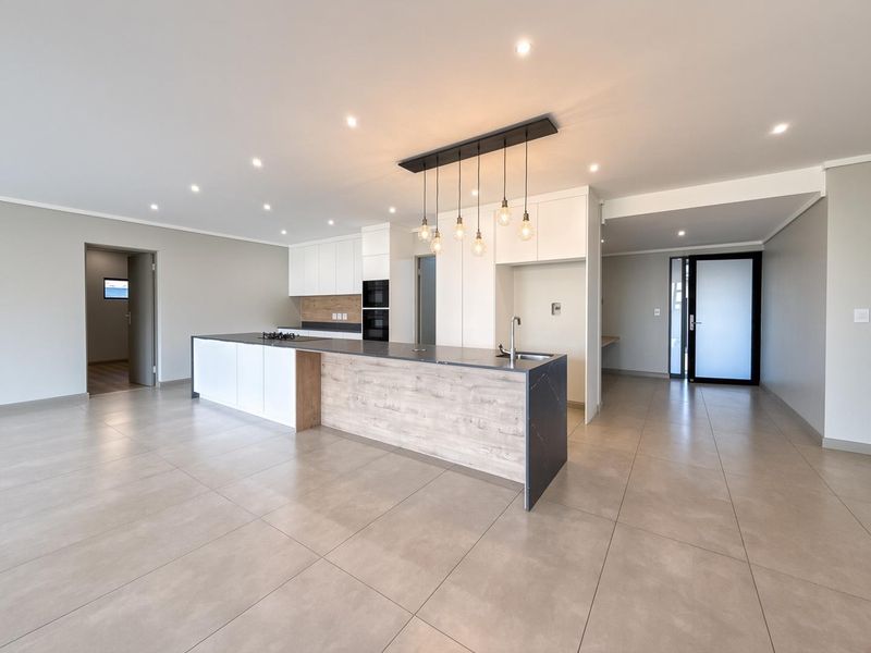 Modern open-plan kitchen featuring a large island with integrated hob, sleek cabinetry, built-in oven, and neutral tiled flooring in a spacious, well-lit area.