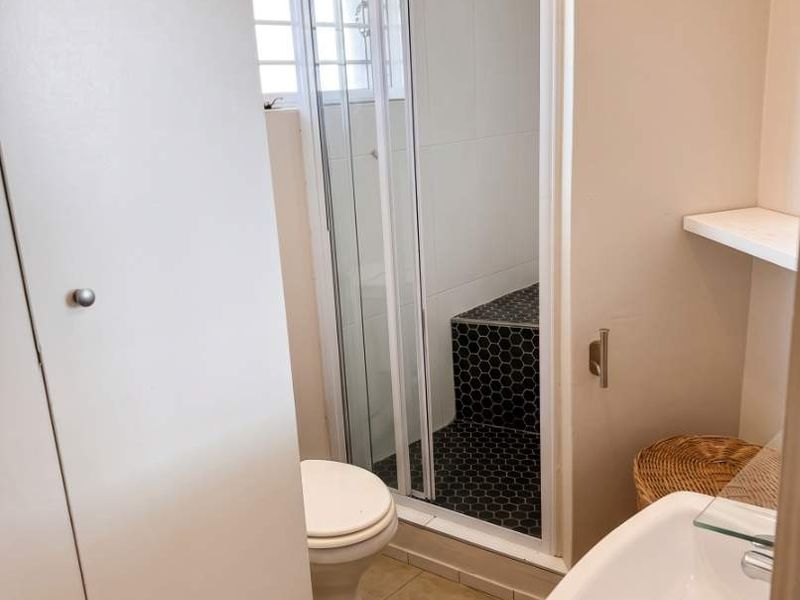 A functional bathroom featuring a shower enclosure, pedestal basin, toilet, and built-in storage cupboard with neutral wall finishes and tiled flooring.