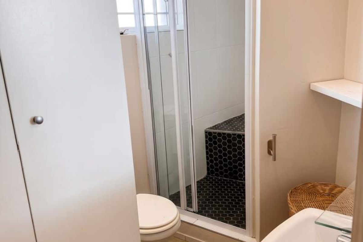 A functional bathroom featuring a shower enclosure, pedestal basin, toilet, and built-in storage cupboard with neutral wall finishes and tiled flooring.