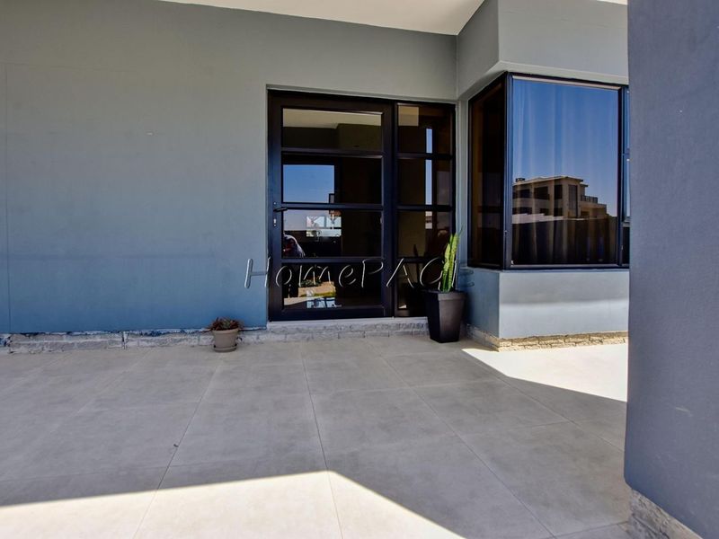 A covered patio area featuring large format floor tiles, a modern aluminium framed glass door, and a bay window with dark frames.