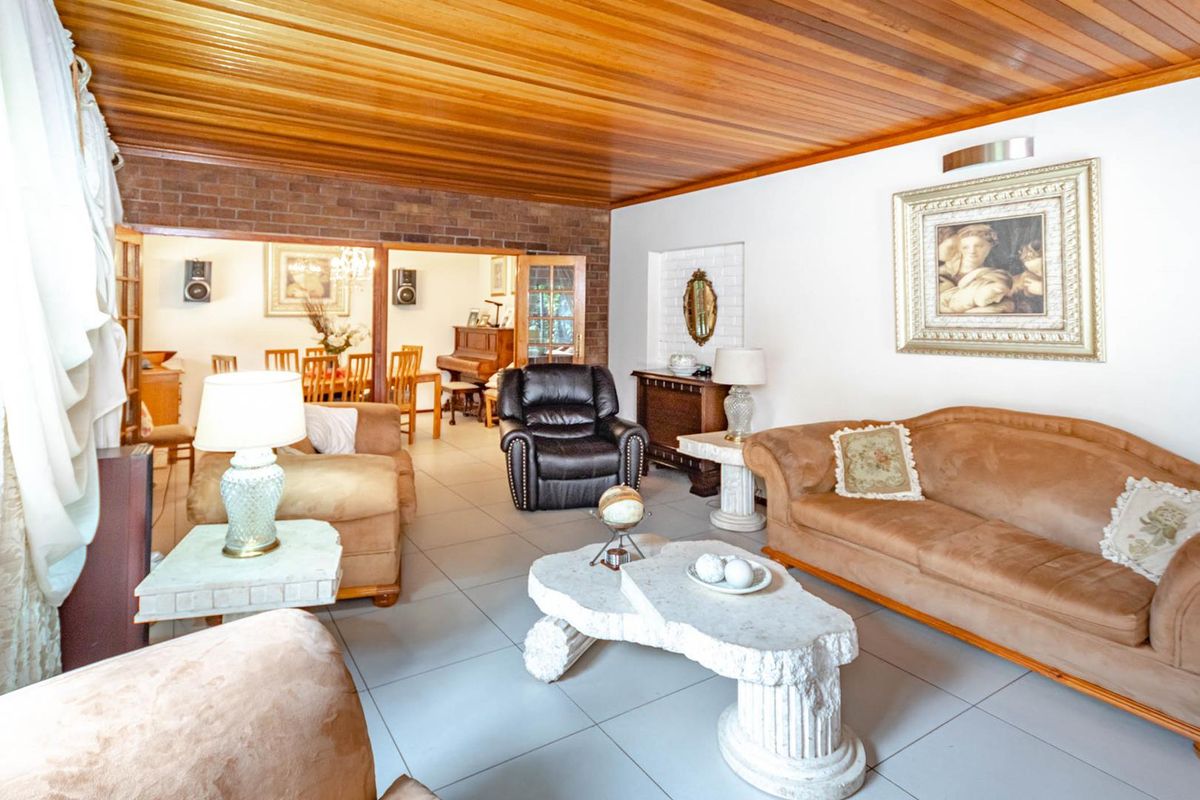 Spacious living area featuring a warm timber-clad ceiling, tiled flooring, and an exposed brick feature wall leading into an adjacent dining space.