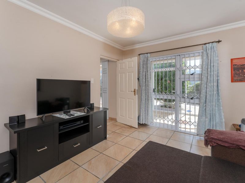 A living room featuring tiled flooring, a ceiling pendant light, and a sliding door with a security gate leading to the exterior.