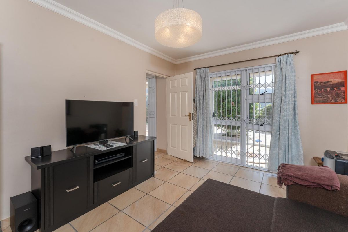 A living room featuring tiled flooring, a ceiling pendant light, and a sliding door with a security gate leading to the exterior.