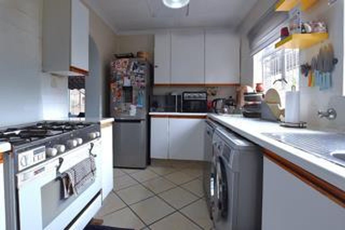 A functional kitchen featuring white cabinetry, gas stove, tiled flooring, and ample counter space, offering a practical layout for daily meal preparation.
