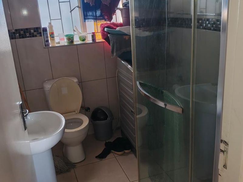 Compact bathroom featuring a pedestal basin, toilet, and glass shower enclosure with tiled finishes throughout.